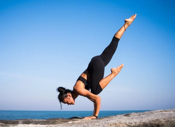 balance lady doing a yoga stretch on a rock by the water