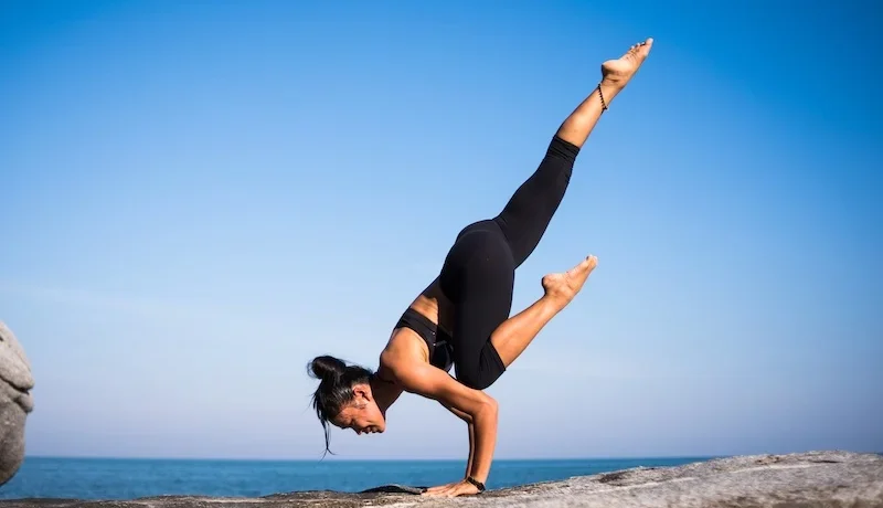 lady doing a yoga stretch on a rock by the water