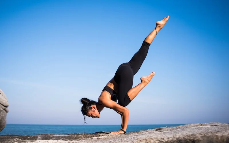 lady doing a yoga stretch on a rock by the water
